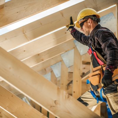 Construction Worker on Duty. Caucasian Contractor and the Wooden House Frame. Industrial Theme.